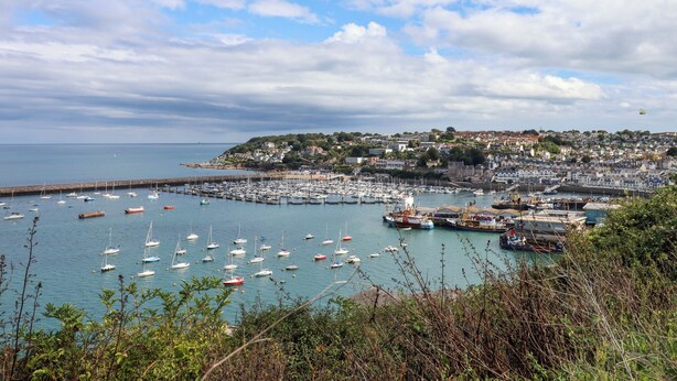 Une ville côtière dotée d’un port de plaisance rempli de bateaux, d’une jetée et d’un quartier bâti sur une colline.