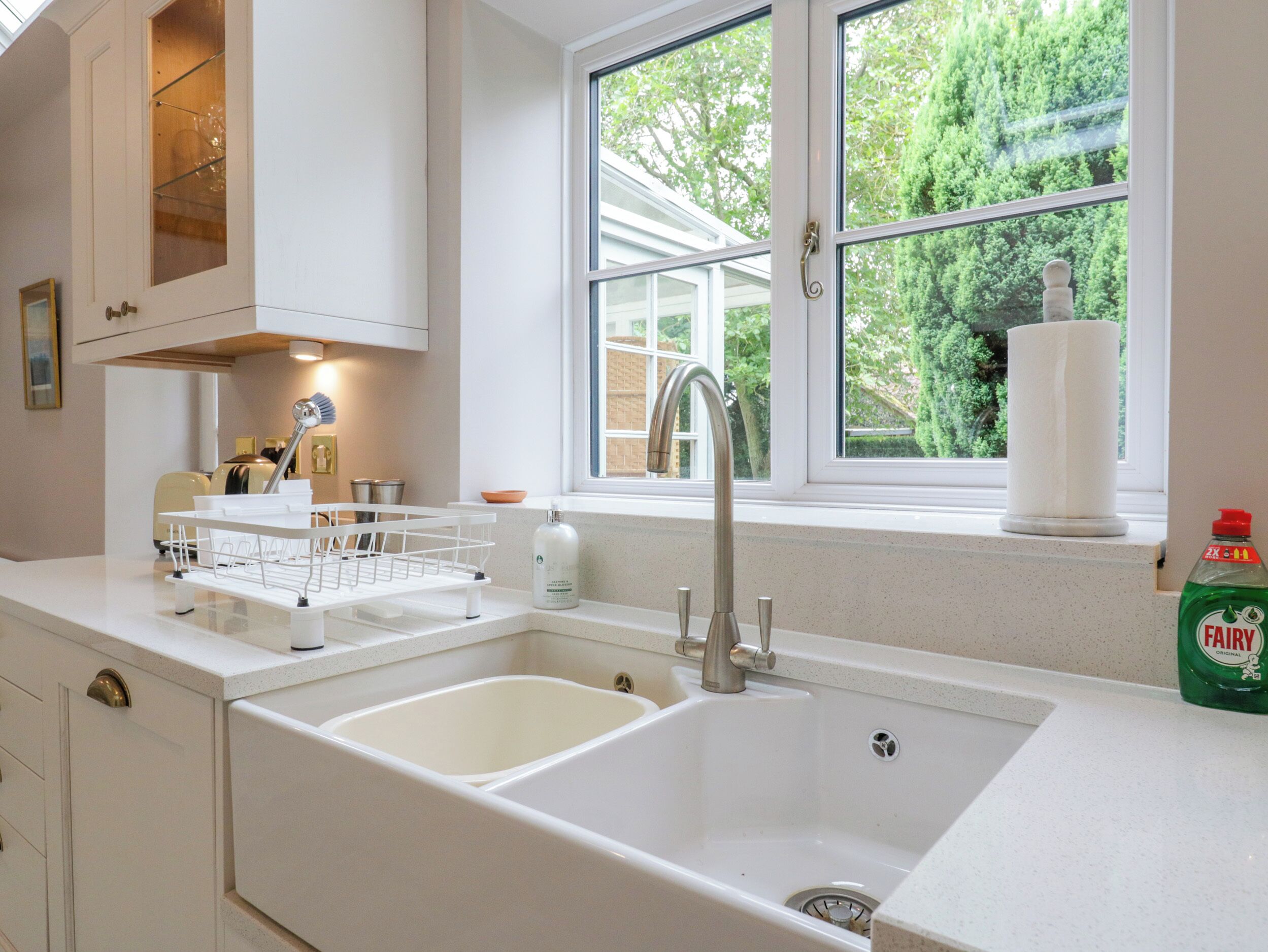 A modern kitchen with a double sink, a window with a view of greenery, and a dish rack.