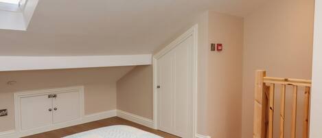 Une chambre avec un puits de lumière, une porte en bois, une armoire blanche et un tapis à motifs.