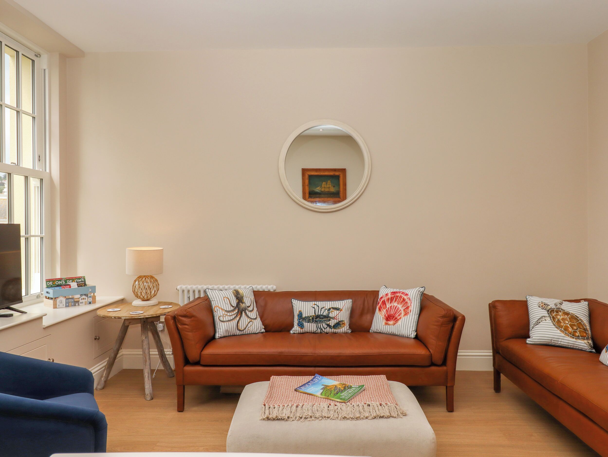 Een woonkamer met een bruine leren bank, een ronde spiegel en een bijzettafeltje met een lamp.