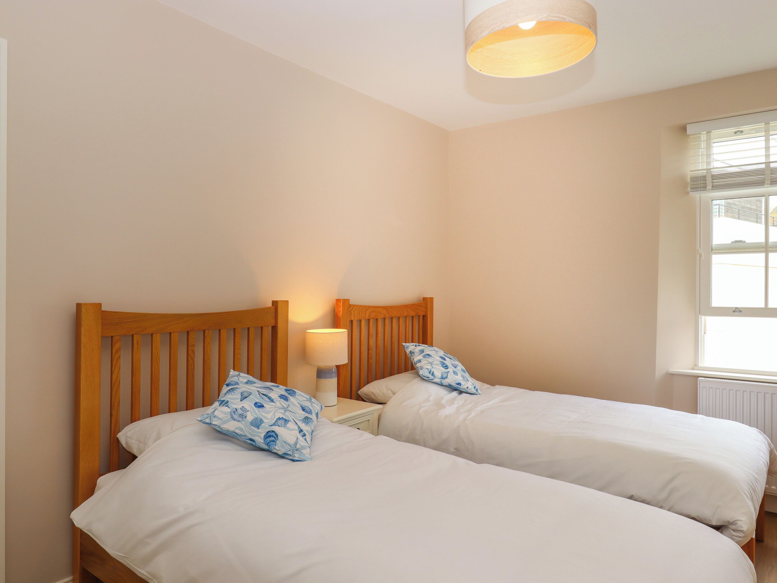Een slaapkamer met twee eenpersoonsbedden, een nachtkastje met een lamp en een raam met zonwering.