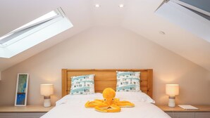 A bedroom with a sloped ceiling, skylights, a bed with two pillows, a bedside lamp, a map on the wall, and a laptop on the nightstand. - 2 Sea Otter House (Teignmouth)