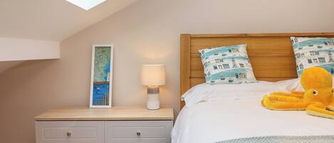 A bedroom with a sloped ceiling, a wooden headboard, a bed with white bedding, a lamp, a map artwork, a plush octopus toy, and a blue patterned throw.