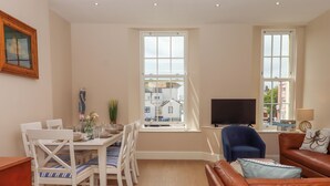A living room with a dining area, a television, and a window with a view of buildings. - 2 Sea Otter House (Teignmouth)