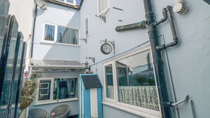 A courtyard with a blue and white house, a clock, and a small garden area with a table and chairs. - 3 Anchor Cottage (Whitby)