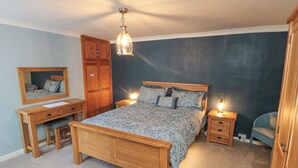 A bedroom with a wooden bed, a desk, a chair, a dresser, and a mirror. - 3 Anchor Cottage (Whitby)