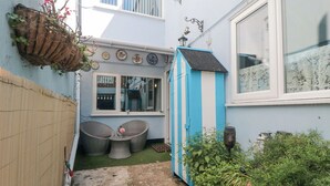 A narrow courtyard with a blue and white shed, wicker chairs, and a hanging plant basket. - 3 Anchor Cottage (Whitby)