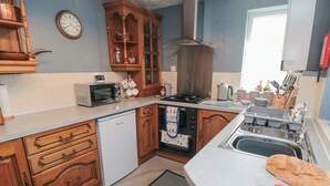 A kitchen with wooden cabinets, a microwave, a stove, and a sink. - 3 Anchor Cottage (Whitby)