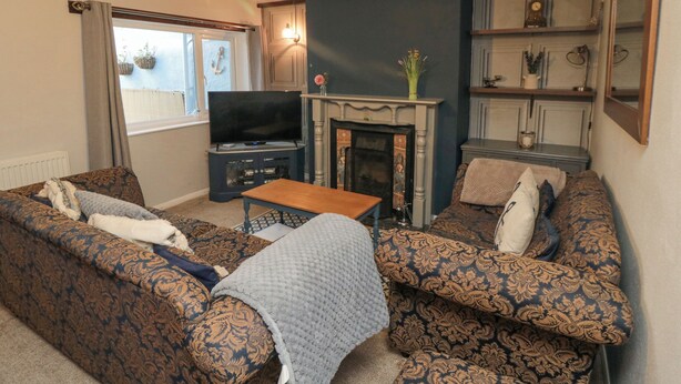 A living room with patterned sofas, a television, a fireplace, and a ceiling light fixture. - 3 Anchor Cottage (Whitby)