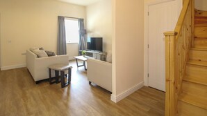 A living room with a sofa, a TV, a small table, and a staircase. - Doncaster Cottage (Oswestry)