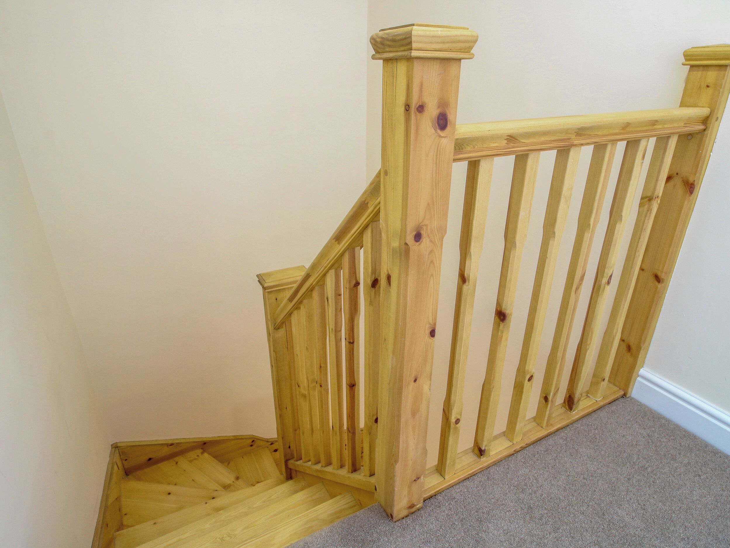 A wooden staircase with a handrail and a carpeted landing.