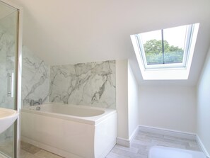 Un baño moderno con pared de mármol, bañera independiente y tragaluz.