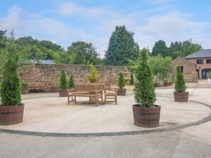 Un patio con un muro de piedra, un banco de madera y varios árboles perennes en macetas.