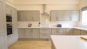 A modern kitchen with light grey cabinets, a built-in oven, a kettle, and a toaster on the countertop. - Doncaster Cottage (Oswestry)