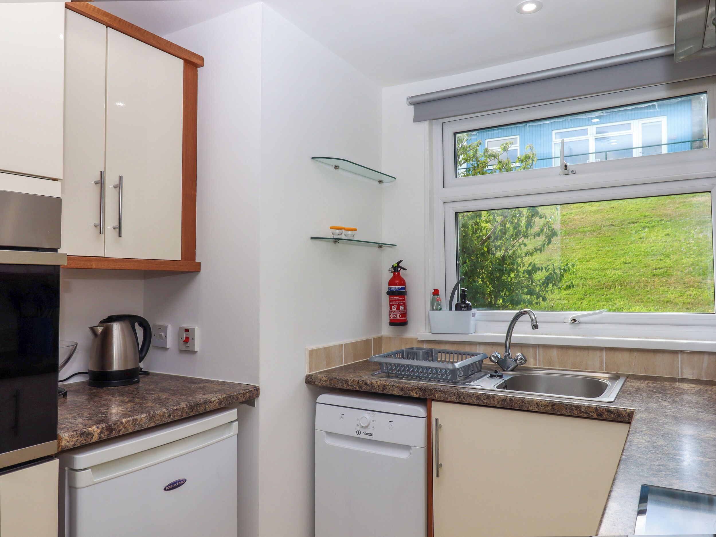 A modern kitchen with white cabinets, a granite countertop, a dishwasher, and a window with a view of greenery.