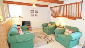 A cozy living room with green sofas, a television, and a wooden ceiling. - Y Stabl (Llanbedr)