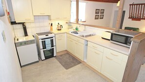 A compact kitchen with white cabinets, a built-in oven, a microwave, and a sink. - Y Stabl (Llanbedr)