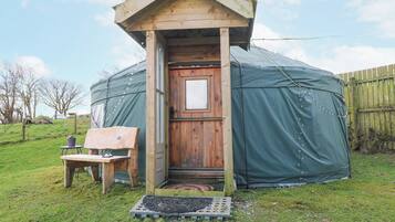 Una estructura de madera con una puerta, un banco y una pequeña mesa afuera.