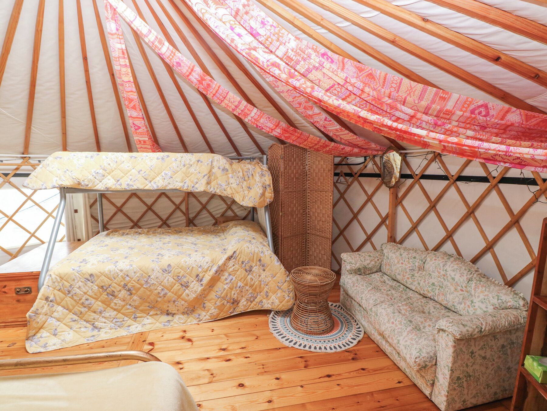 Interior acogedor de una yurta con una cama, un taburete tejido y un sofá.