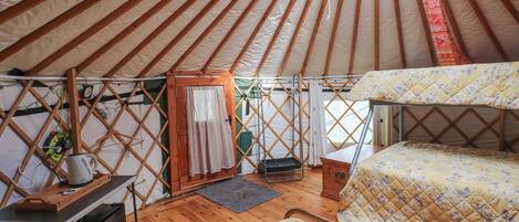 Un interior acogedor de una yurta con una cama, una mesita y un calentador.