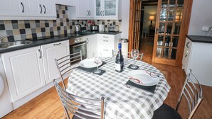 Une cuisine avec des meubles blancs, une nappe à carreaux et une bouteille de vin.