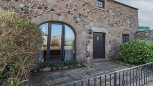 A stone building with a black door, a large arched window, and a small window above the door. - Aubretia Trail (Wooler)