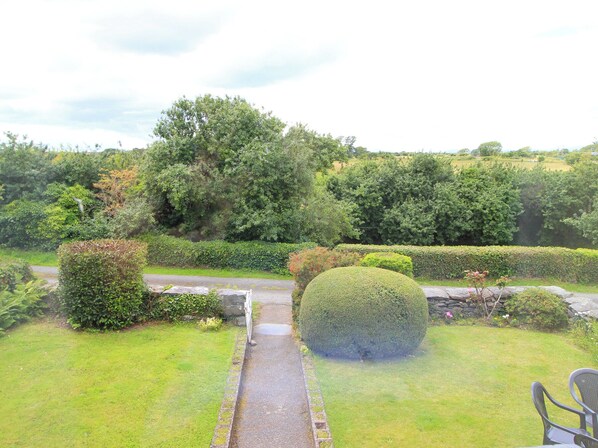 A garden pathway leading to a seating area with a view of a lush, green landscape. - The Farmhouse (Llanbedr)