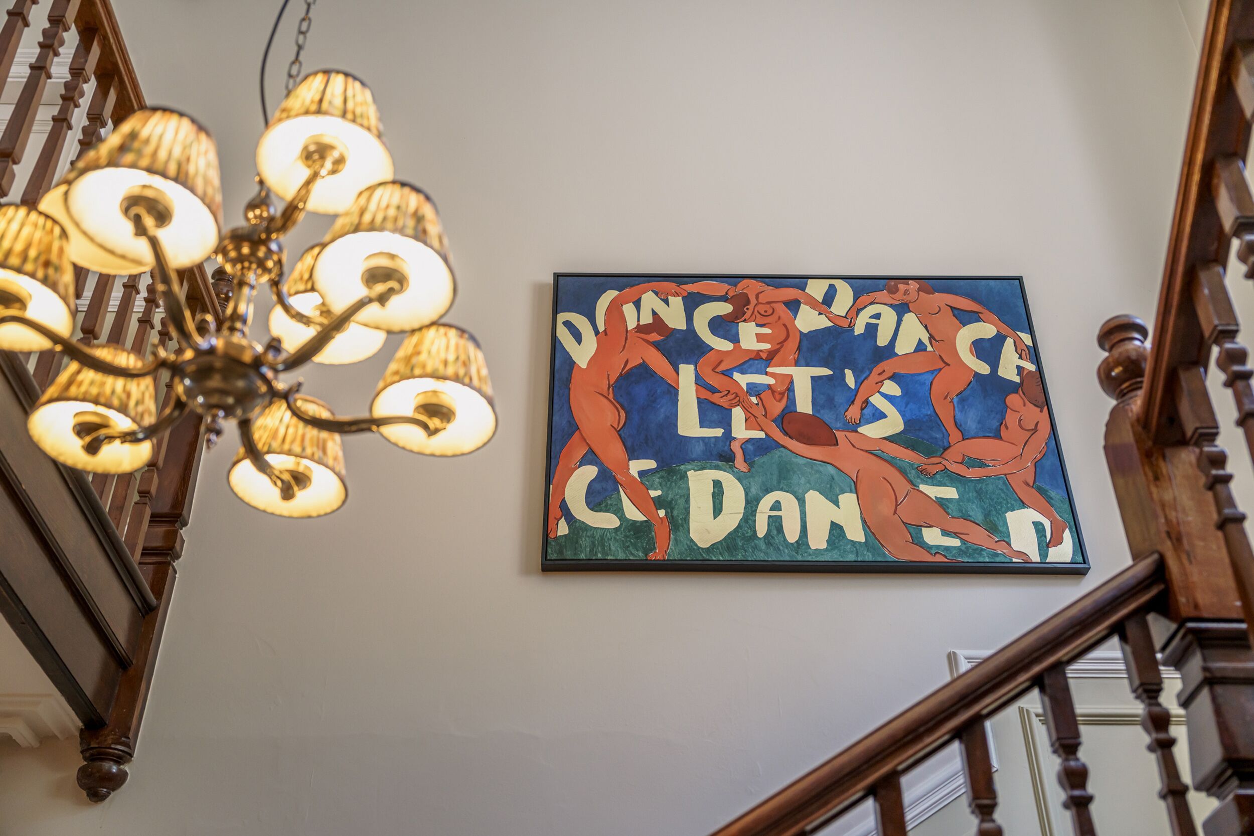 Een kroonluchter en een kunstwerk met dansmotieven aan een muur.
