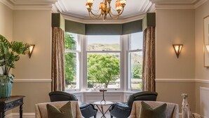 A room with two leather armchairs, a small table, and a bay window with curtains. - Leathes Head Country House (Keswick)