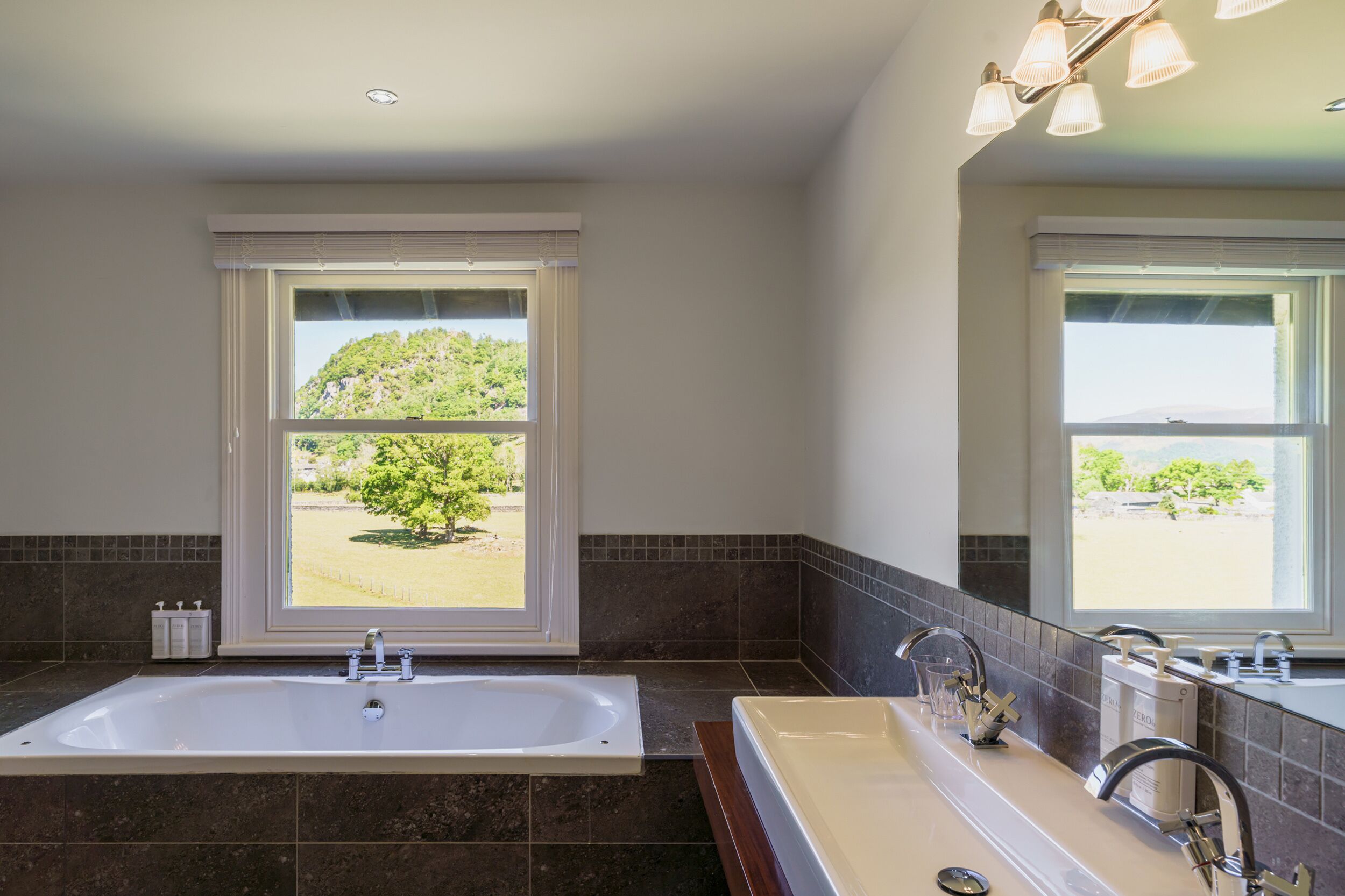 A bathroom with a large bathtub, a sink, and a window with a view of greenery.
