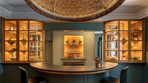 A bar area with wooden cabinets displaying glassware and bottles, a central island with seating, and a woven ceiling light fixture. - Leathes Head Country House (Keswick)