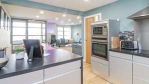 A modern kitchen with stainless steel appliances, a dining area with a large table, and a living room with a sofa and TV. - 2 The Quay (Pentraeth)