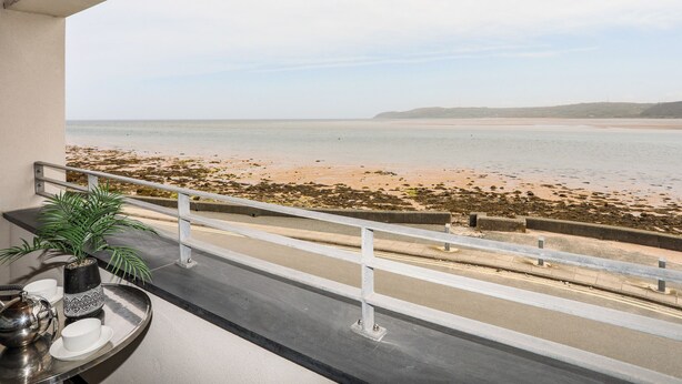 A balcony with a view of the beach, a metal table with a plant and a teapot, and a railing. - 2 The Quay (Pentraeth)