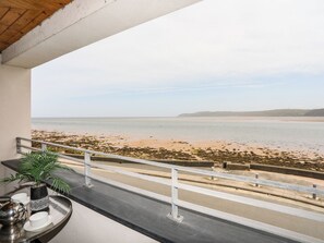 Un balcone con vista sulla spiaggia, un tavolo in metallo con una pianta e un bollitore, e una ringhiera.