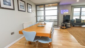A modern living room with a wooden dining table, light blue chairs, a sofa, and a TV. - 2 The Quay (Pentraeth)