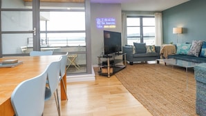 A modern living room with a TV, sofa, and dining area. - 2 The Quay (Pentraeth)