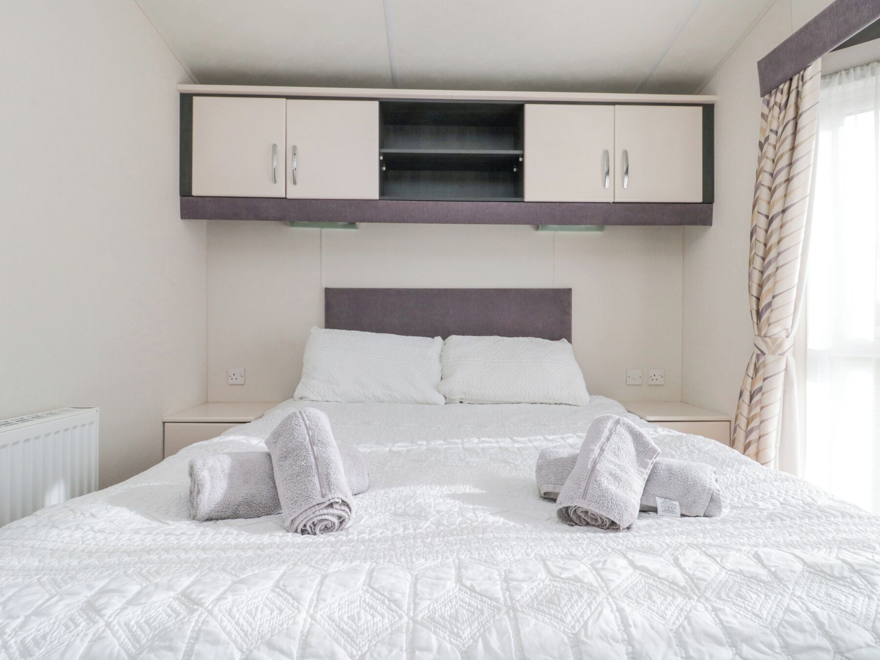A hotel room with a bed, two nightstands, a wardrobe, and a window with curtains.