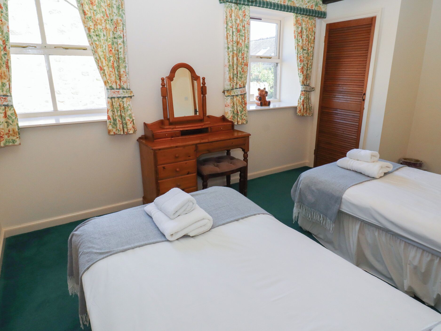 Une chambre d’hôtel avec deux lits, une commode en bois, un miroir et des rideaux à motifs floraux.