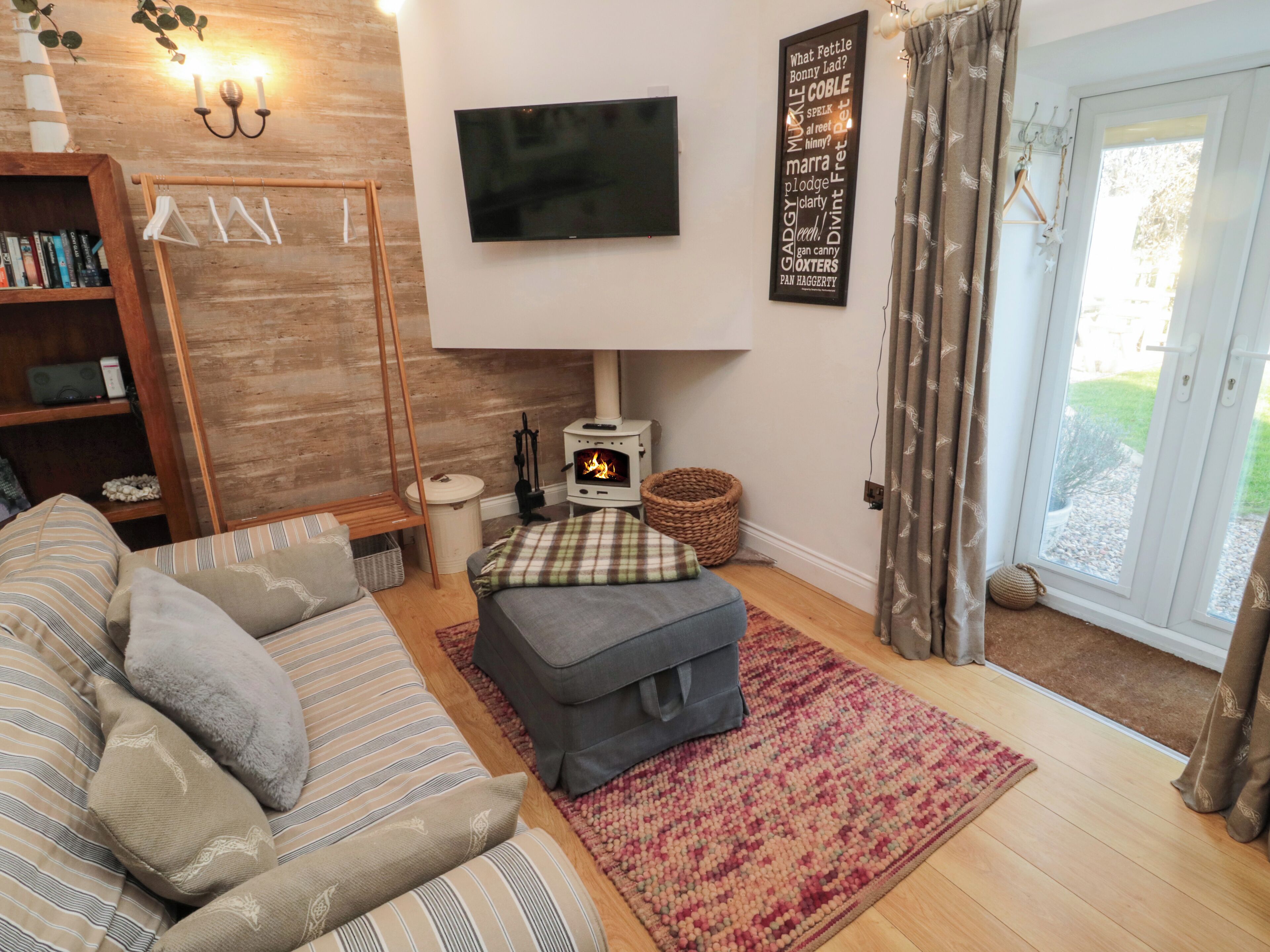 Een gezellige woonkamer met een bank, een poef en een flatscreen televisie aan de muur.