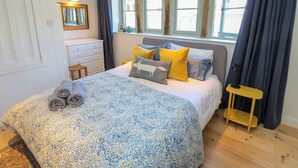 A bedroom with a bed, a dresser, a mirror, a window with curtains, and a small table. - Cobbles Cottage (Hebden Bridge)