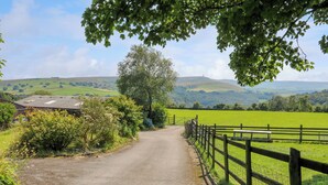 A rural road leading through a green landscape with a fence on one side and a building on the other. - Cobbles Cottage (Hebden Bridge)
