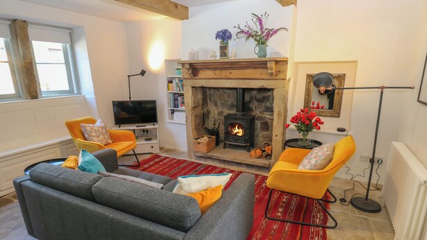 A cozy living room with a stone fireplace, two sofas, a television, and a bookshelf. - Cobbles Cottage (Hebden Bridge)