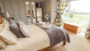 A bedroom with a bed, a wooden bench, a mirror, and a window with curtains. - Morva (New Quay)