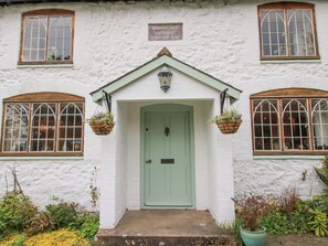 Un bâtiment blanc avec une porte verte, deux fenêtres à cadres en bois et des jardinières suspendues.