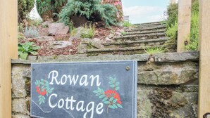 Segnaletica per Rowan Cottage, con un muro in pietra e gradini che conducono alla costruzione.