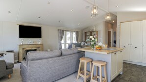 A modern living room with a grey sofa, a small kitchen area with a bar stool, and a fireplace. - Bethany's Retreat (Wemyss Bay)