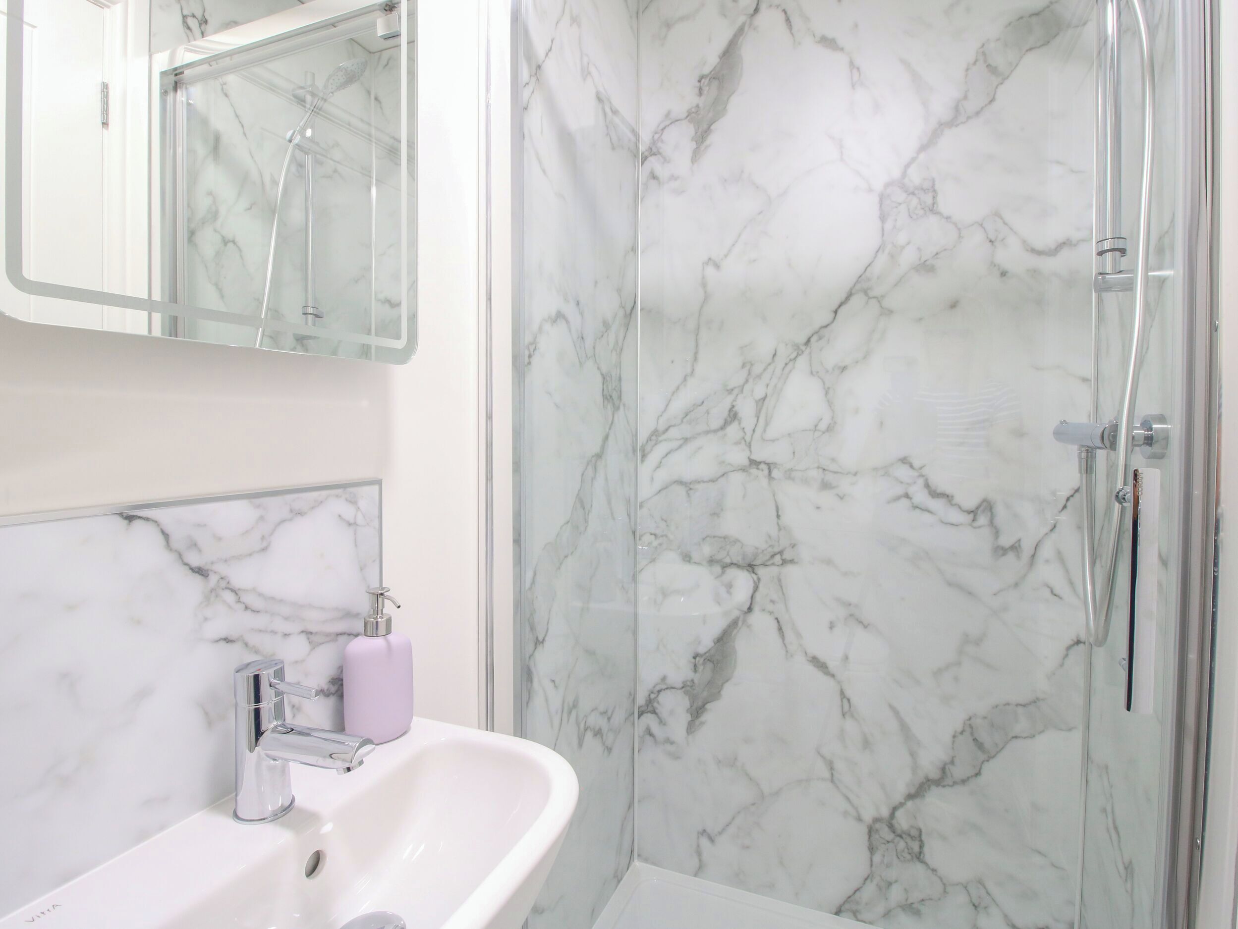 A bathroom with a marble shower wall, a sink with a mirror, and a toilet.