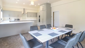 Une cuisine moderne avec des meubles blancs, un îlot central et un coin repas comprenant une table et des chaises.