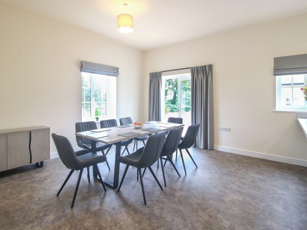 Un espace repas comprenant une table rectangulaire, six chaises, un buffet en bois et un luminaire suspendu au plafond.