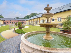 Une cour intérieure avec une fontaine centrale, un bâtiment en briques et une pelouse bien entretenue.